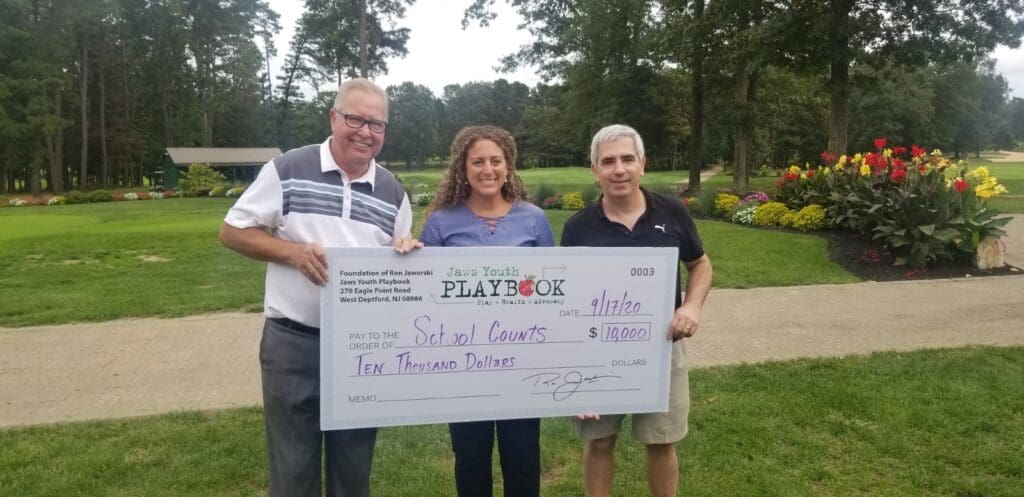 Two men and a woman holding a check in front of a golf course.