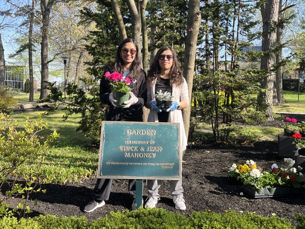 Two women standing in front of a sign in a garden.