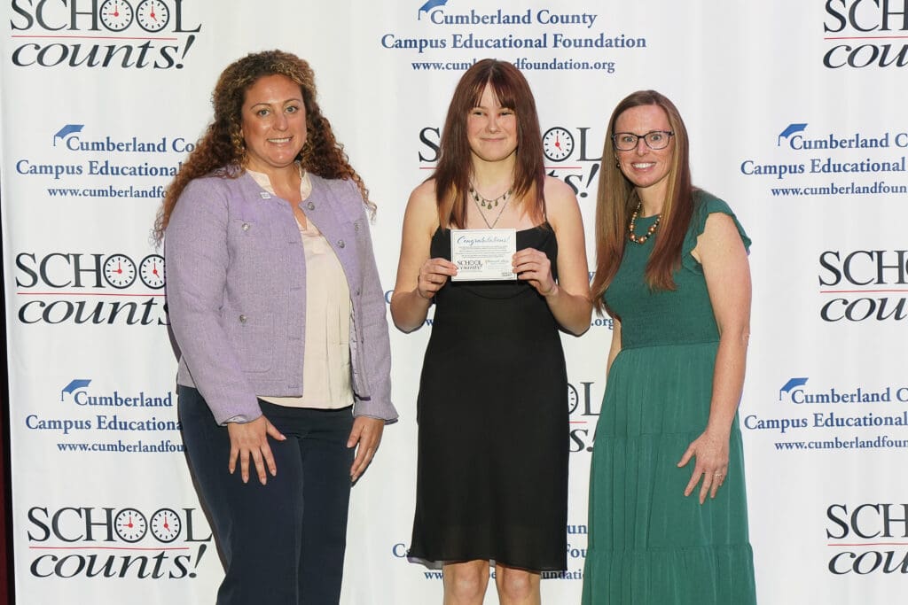 Three women posing at an award event, one holding a certificate.