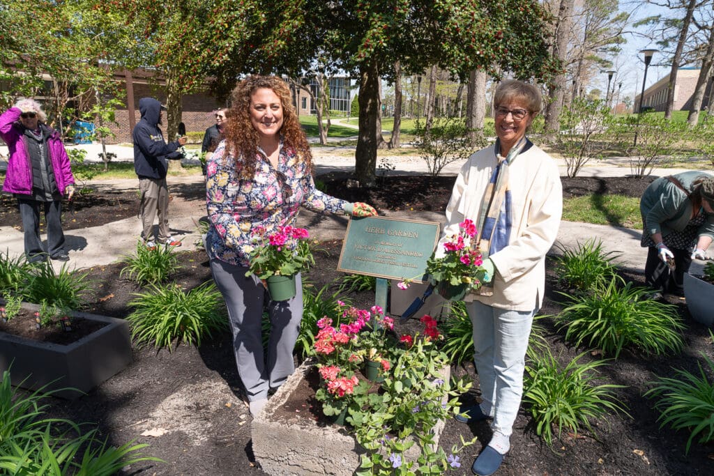 Two women planting flowers around a tree in a park on a sunny day.