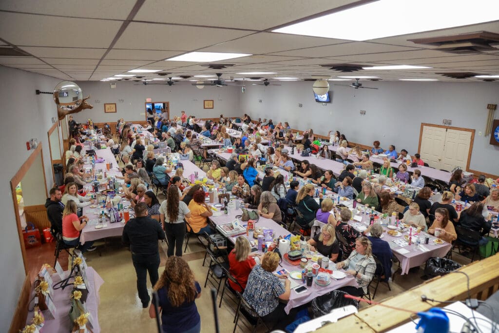 Large group gathered in a community hall for a shared meal event.