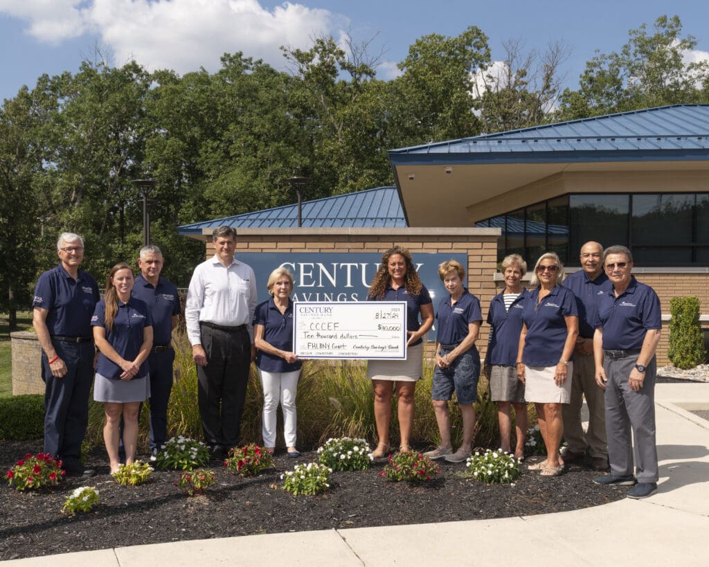 Group of people posing outside a building with a large check.