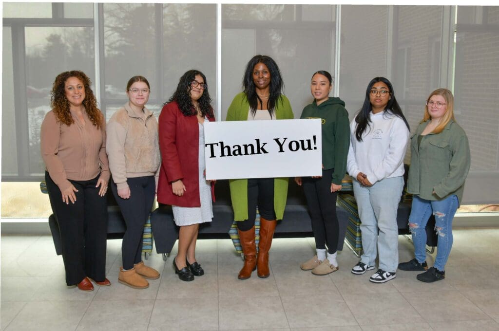 Group of seven diverse people holding a 'Thank You!' sign indoors.