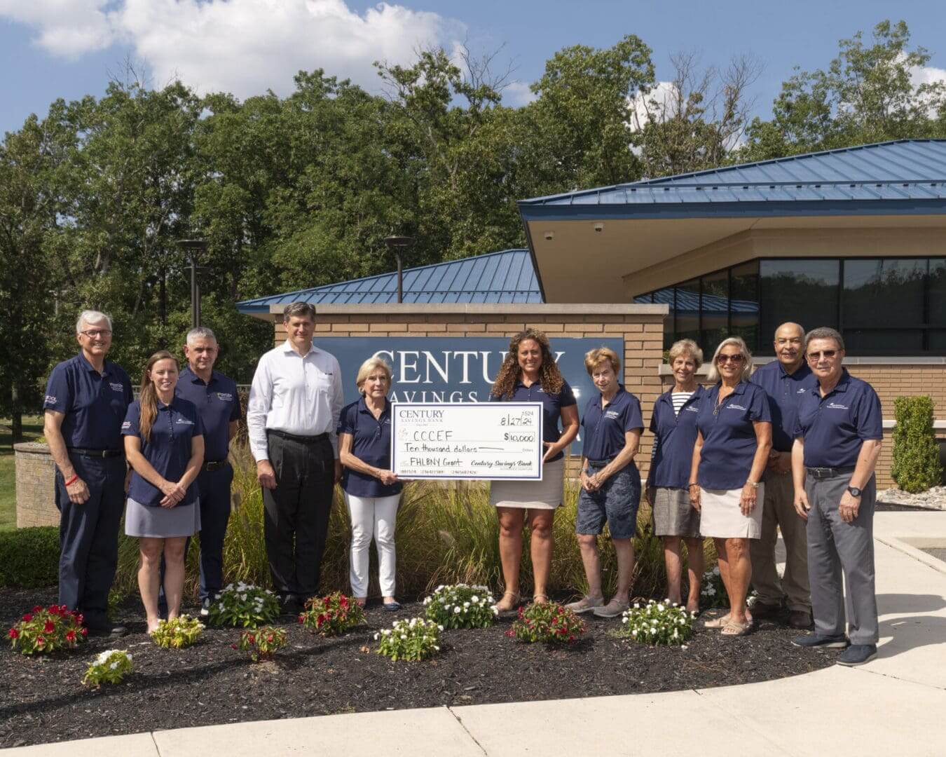 Group of people posing with a large check outside a building.
