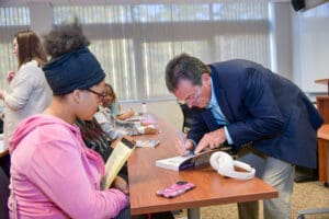 Man signing book for student in classroom.