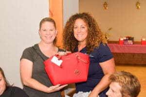 Two women holding a red handbag, smiling.