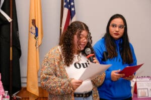 Two people speaking at event with flags