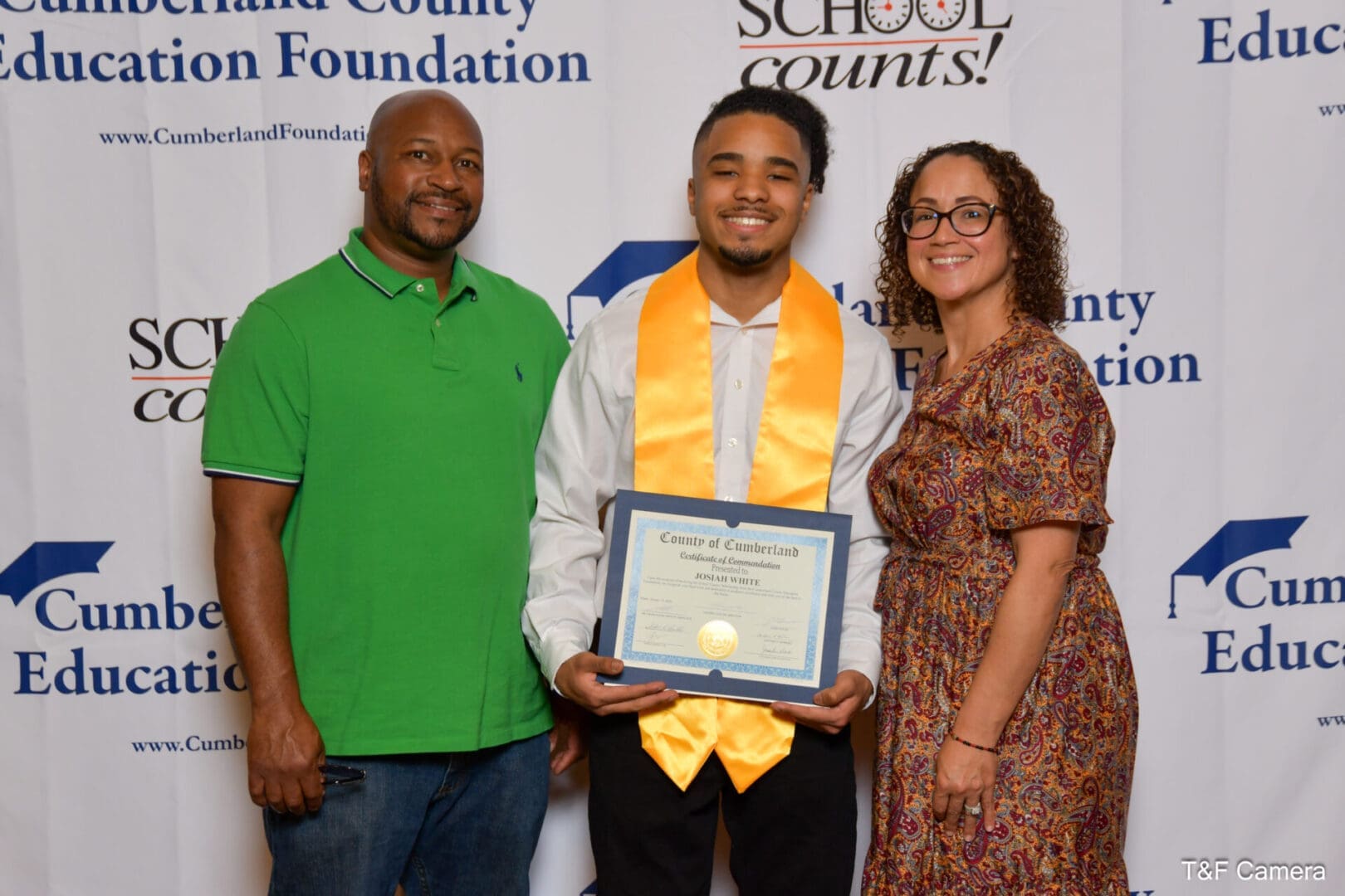 Smiling graduate holding certificate with two adults