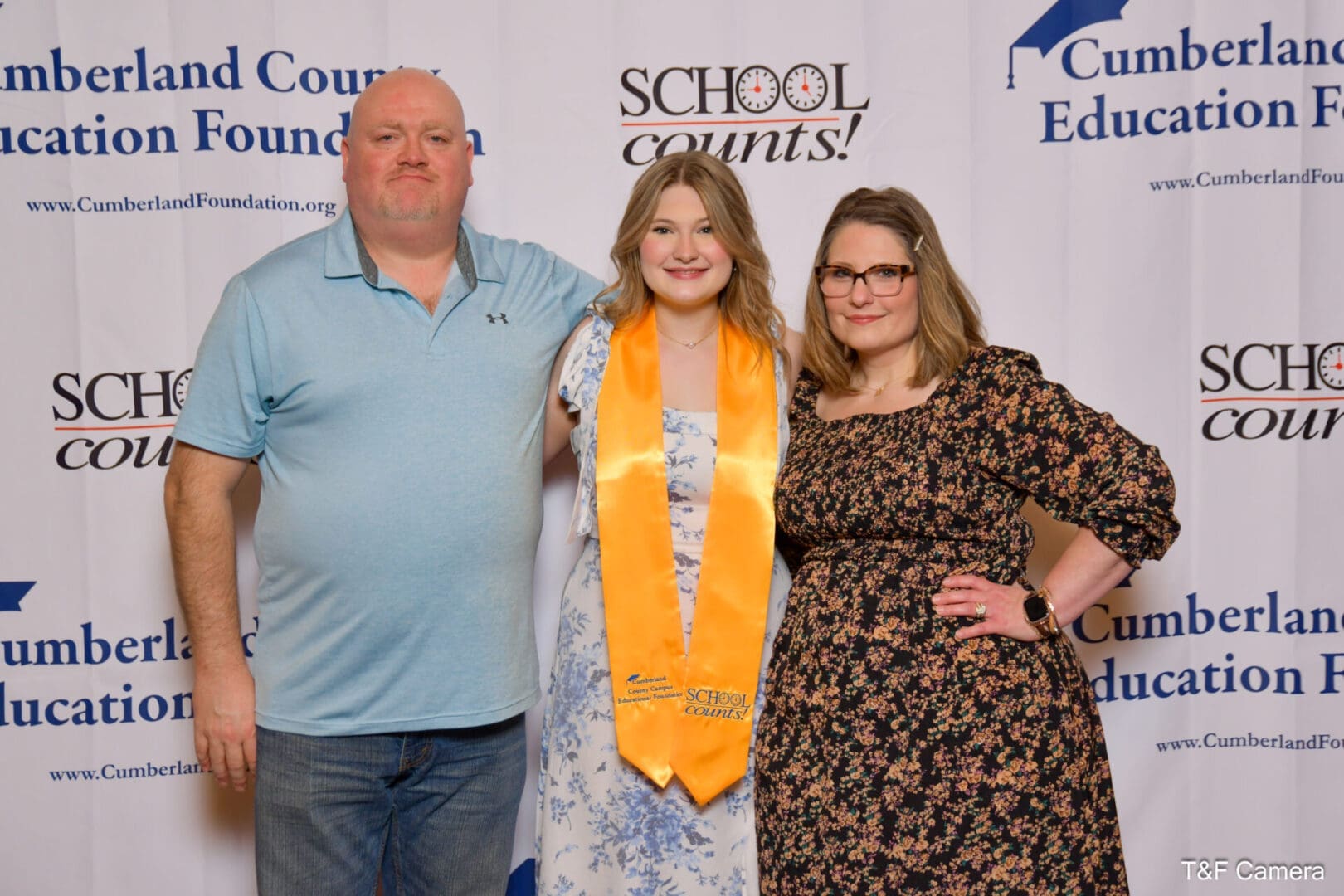 Smiling graduate in yellow stole with parents
